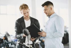 Two men reviewing documents in a motorcycle dealership, discussing a purchase agreement.
